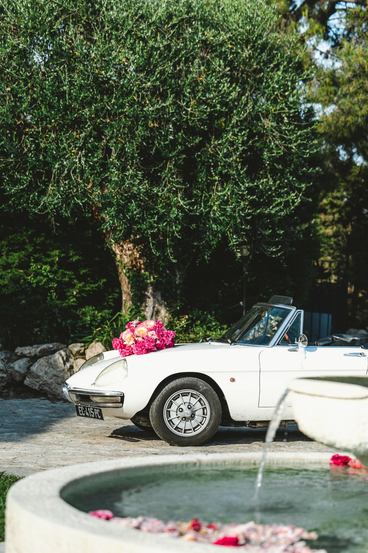 Voiture ancienne fleurie devant la fontaine du Mas Baïeta