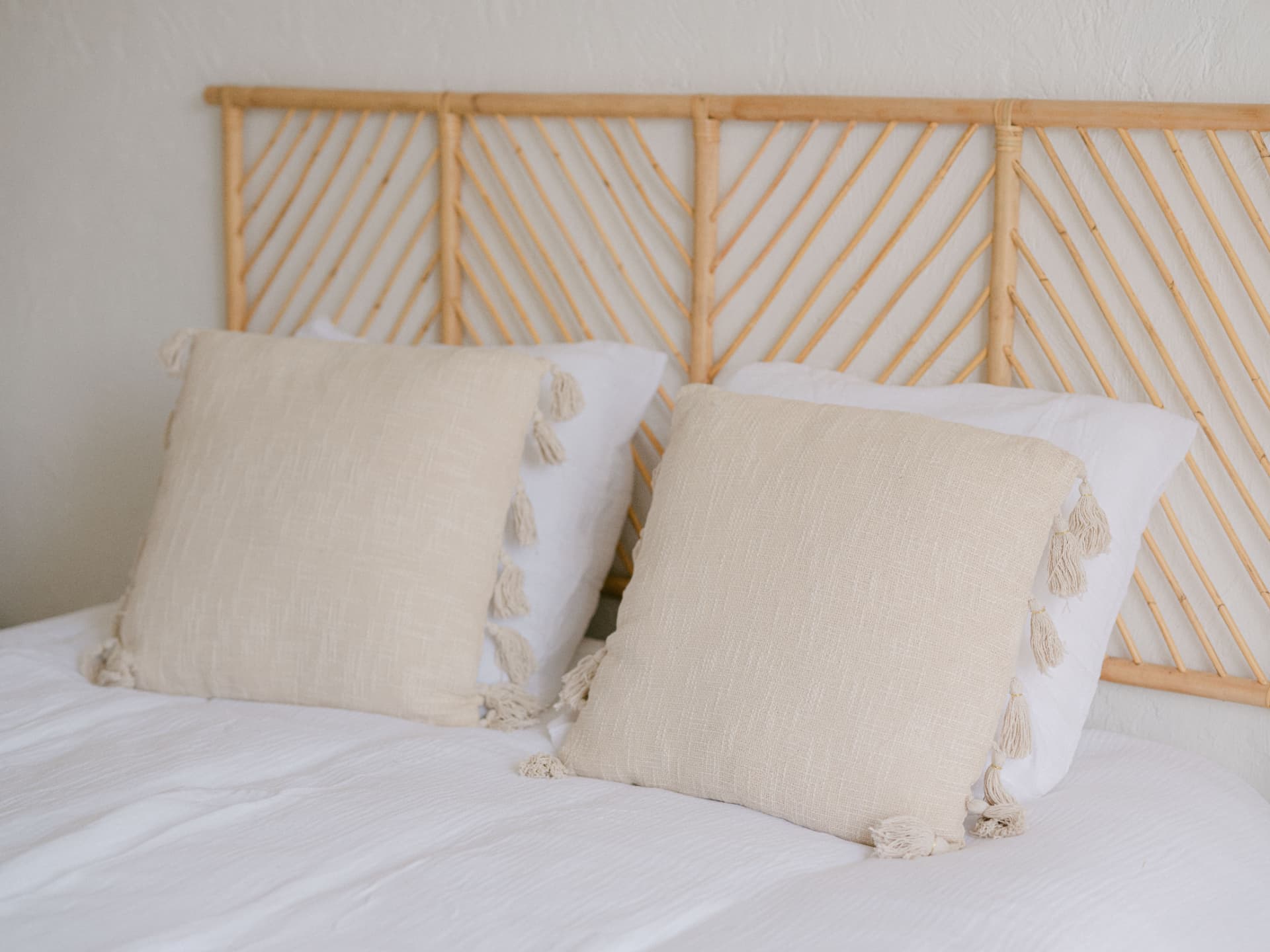 Lit aux draps blancs et coussins beiges, tête de lit en bois clair